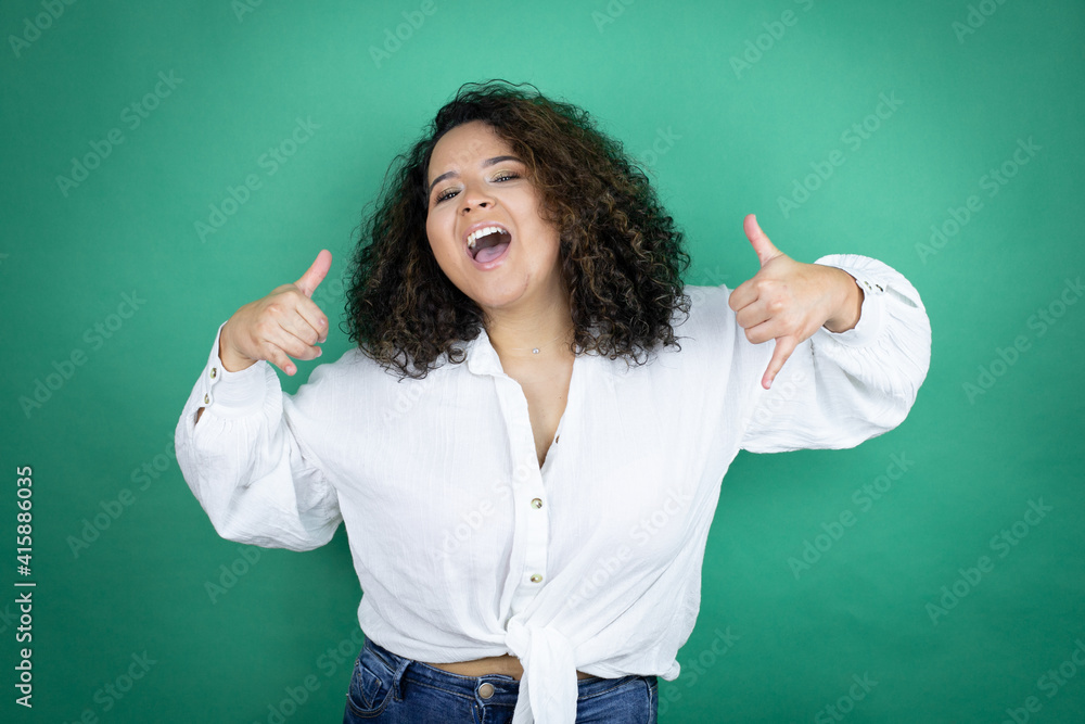 Young african american girl wearing white shirt over green background shouting with crazy expression doing rock symbol with hands up Young african american girl wearing white shirt over green background shouting with crazy expression doing rock symbol with hands up