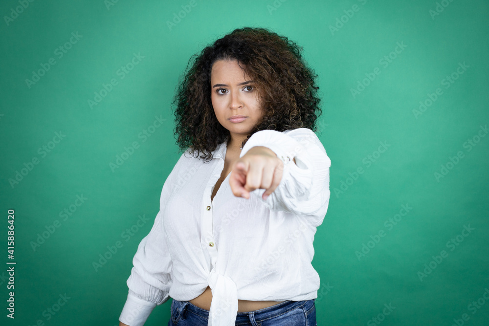 Young african american girl wearing white shirt over green background pointing with finger to the camera and to you, confident gesture looking serious Young african american girl wearing white shirt over green background pointing with finger to the camera and to you, confident gesture looking serious