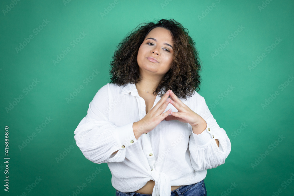 Young african american girl wearing white shirt over green background with Hands together and fingers crossed smiling relaxed and cheerful. Success and optimistic