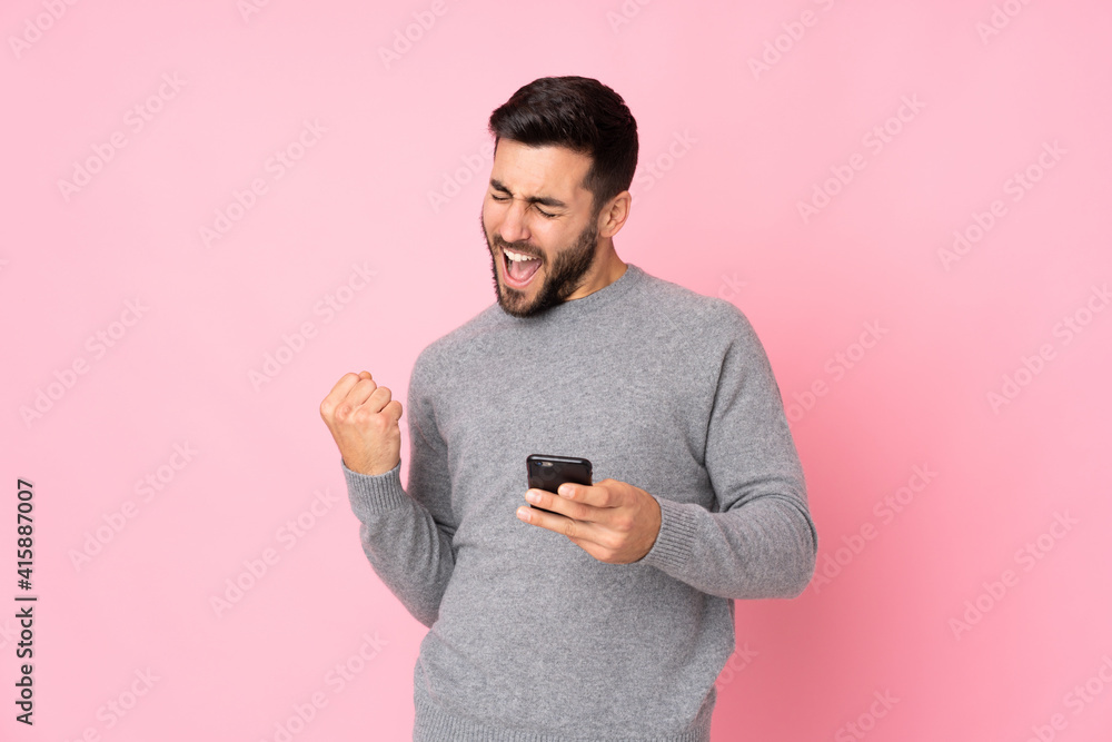Caucasian handsome man over isolated background with phone in victory position Caucasian handsome man over isolated background with phone in victory position