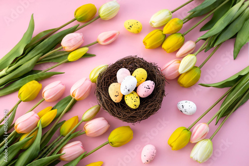 Fototapeta Naklejka Na Ścianę i Meble -  Colorful easter quail eggs in nest and tulips on pink background with . Flat lay. Spring composition. Happy easter greeting card.