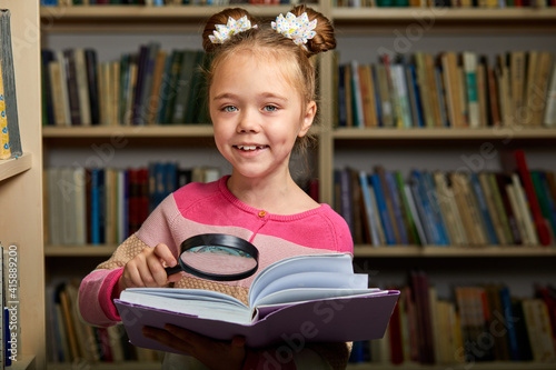 smiling girl using magnifying glass for better reading books, she is enjoying time of education, studying. in library photo