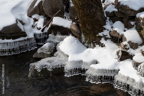Amazing crystal icicle shapes hanging from the edge of snow covered riverbank during winter photo
