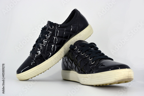 Stylish bright black lacquer shoes located on a white background. Moccasins made of genuine leather with bullshit and black wide laces. Women's sneakers on a white tast sole. 