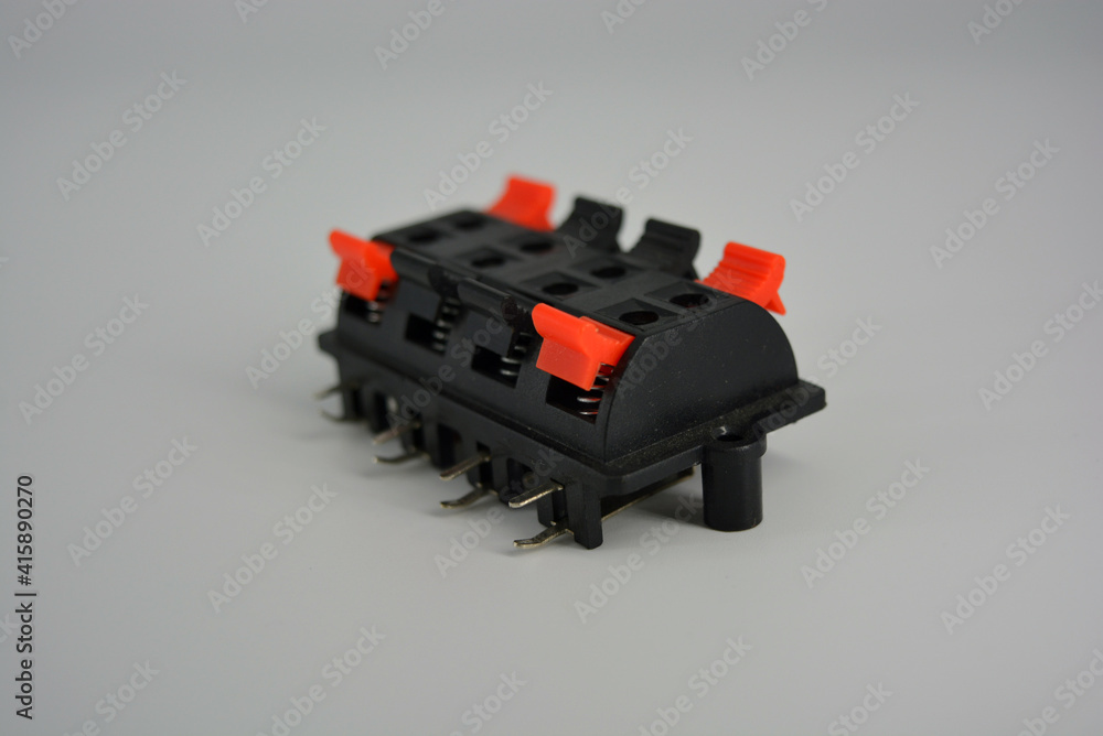 Black electric plastic box for fixing wires with red and black clamps for simultaneous connection of bare wires located on a white plastic background. 