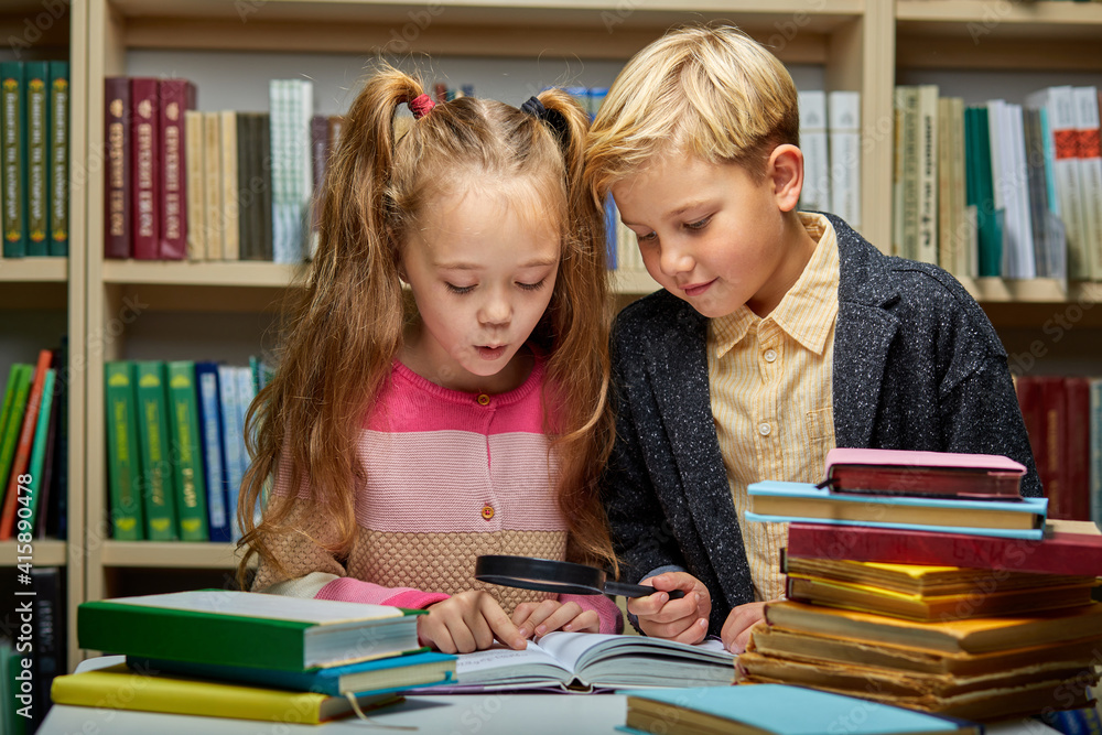 school kids reading book together while sitting at table in library, boy and girl among lots of books, preparing fro school school kids reading book together while sitting at table in library, boy and girl among lots of books, preparing fro school