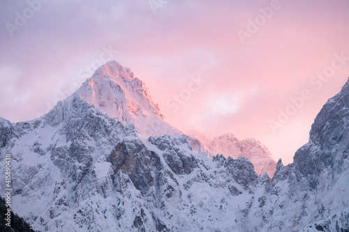 Beautiful close up shot of a pink glowing Mountain top in the Alps at sunset while wind is blowing snow off the Mountain. Power of natural elements in an alpine environment