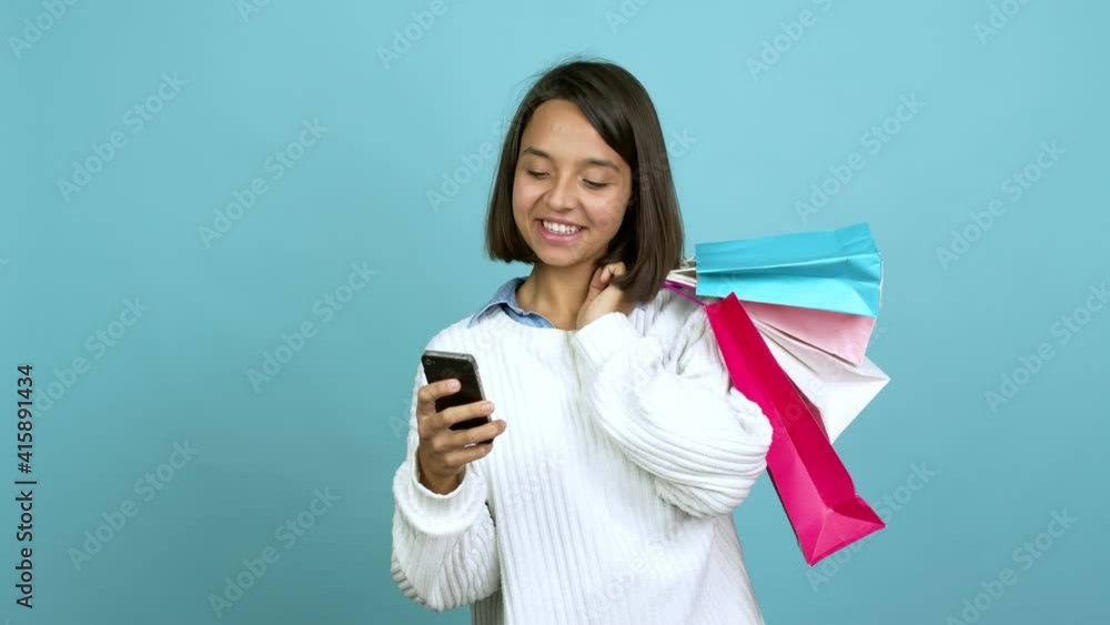 Young brunette woman holding shopping bags while using mobile phone isolated on background Young brunette woman holding shopping bags while using mobile phone isolated on background