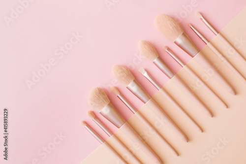 Makeup brushes on pink and beige background. Woman beauty accessory in pastel colors. Flat lay  top view  copy space