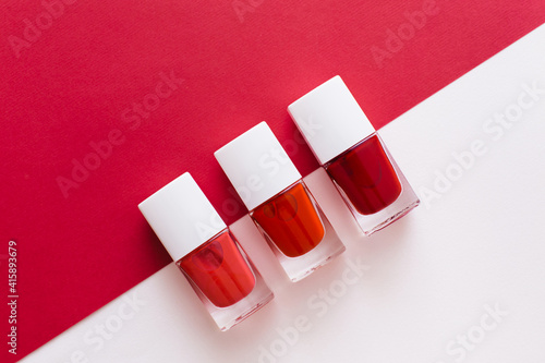 Bottles of red nail polish on red and white background. Manicure and pedicure concept. Flat lay, top view, copy space photo