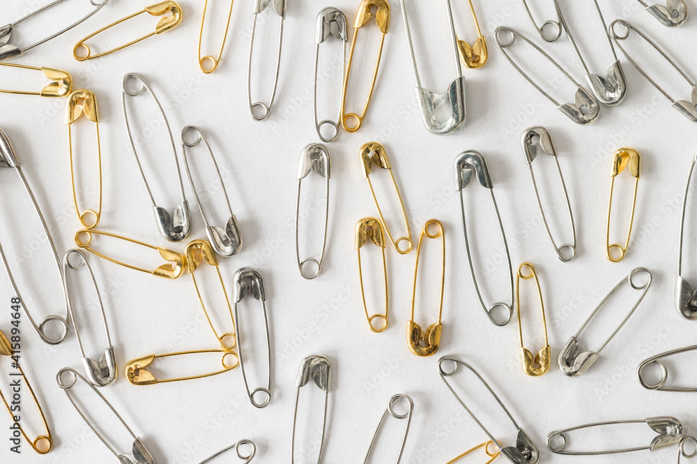 Silver and gold safety pins scattered on a white background Silver and gold safety pins scattered on a white background