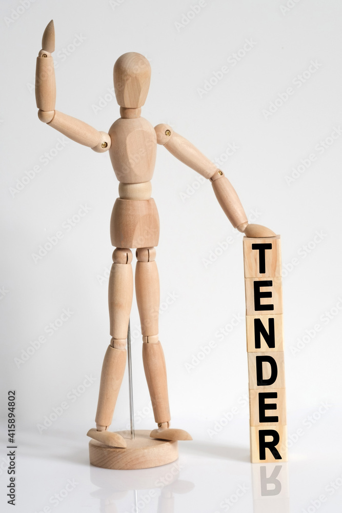 The wooden man raised his hand, and under his left hand he has cubes with the inscription - TENDER The wooden man raised his hand, and under his left hand he has cubes with the inscription - TENDER