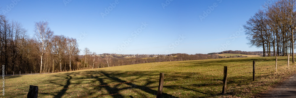 panorama view of countryside with meadows, fence and a village in the distance, blue sky