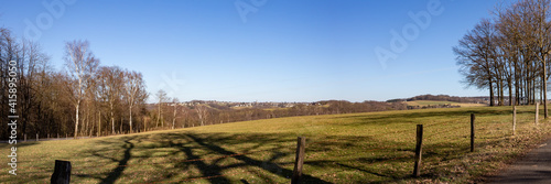 panorama view of countryside with meadows, fence and a village in the distance, blue sky