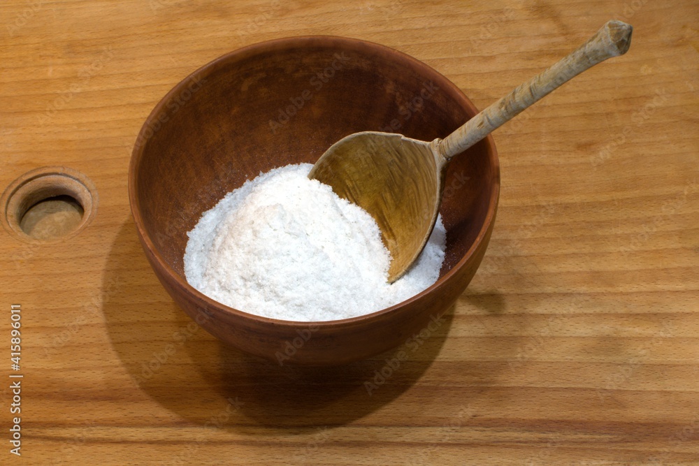 white edible salt in wooden bowl with wooden spoon on wooden cutting board for home cooking
