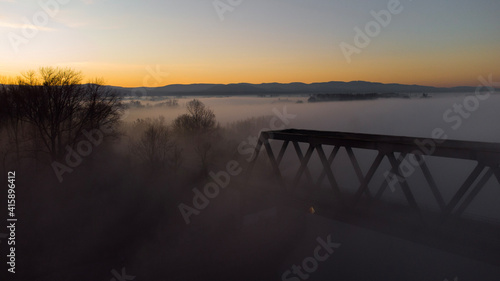 Bridge at Sunrise with a orange sky in the Horizon . The picture was taken by a drone. the River unter the Bridge called Rhein.  scary fog is around the bridge.