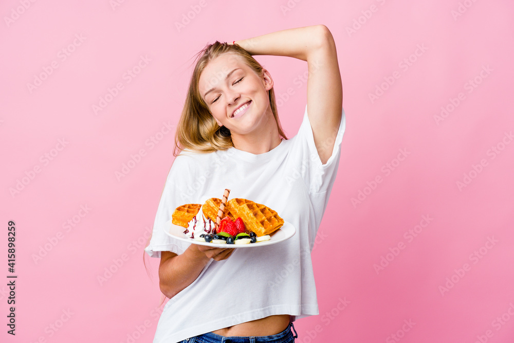 Young russian woman eating a waffle isolated stretching arms, relaxed position.