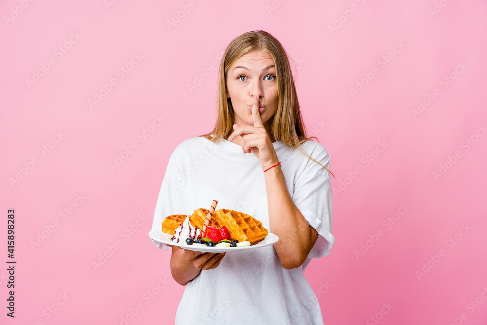 Young russian woman eating a waffle isolated keeping a secret or asking for silence. Young russian woman eating a waffle isolated keeping a secret or asking for silence.