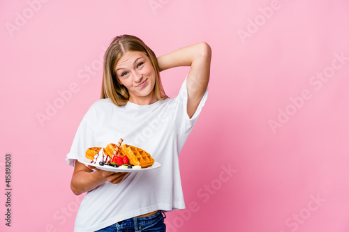 Young russian woman eating a waffle isolated touching back of head, thinking and making a choice.