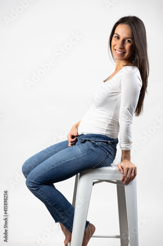 Young stylish adult woman in early pregnancy holds belly and smiles towards camera