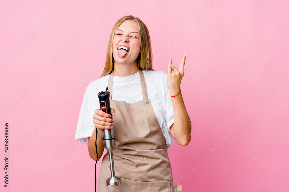 Young russian cook woman holding an electric mixer isolated showing rock gesture with fingers