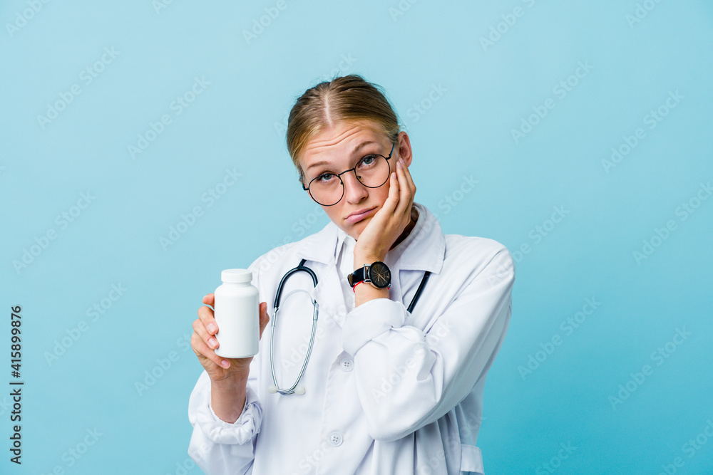 Young russian doctor woman holding pills bottle on blue who is bored, fatigued and need a relax day. Young russian doctor woman holding pills bottle on blue who is bored, fatigued and need a relax day.
