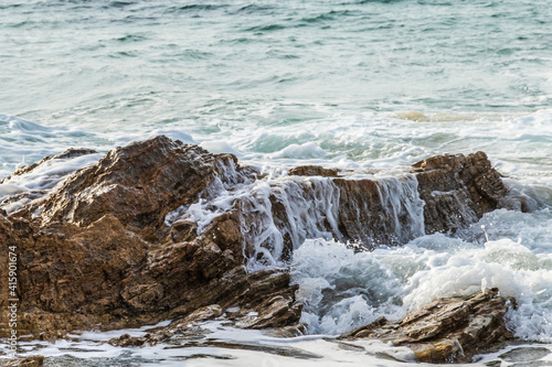 closeup of wave gently flowing over rock on california coastline; water cascading down the side. Pacific ocean in the background. 