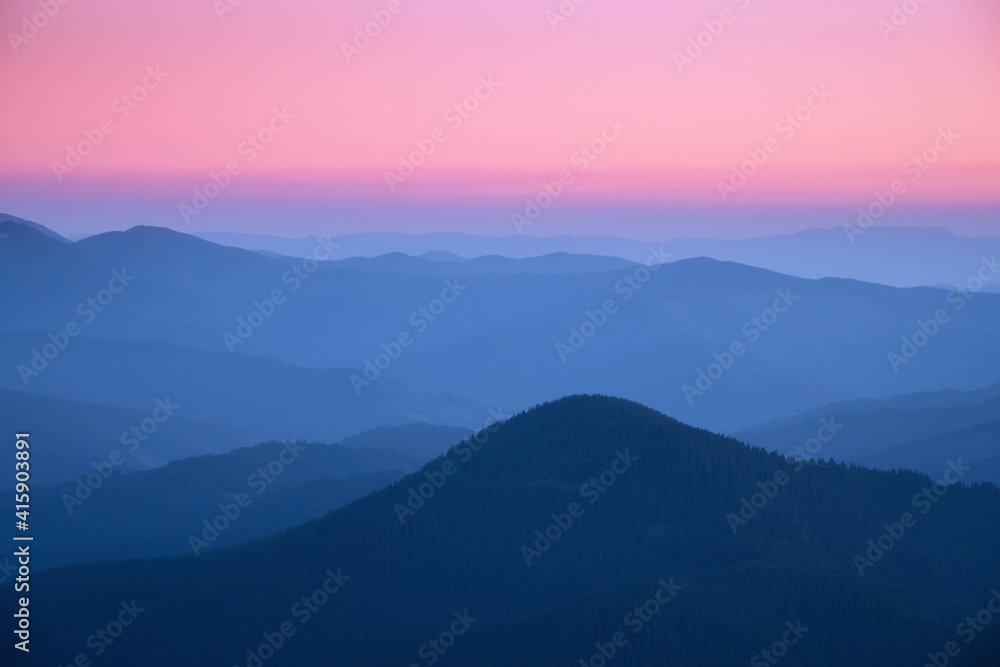 Mountain ridges in fog at sunset in autumn. Beautiful landscape with foggy mountain valley, rocks, forest, pink sky in fall at dusk in blue hour. Aerial view of hills. Top view. Nature background