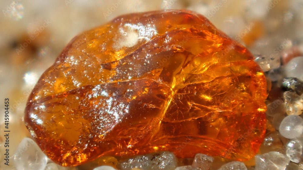Fototapeta premium Close-up of a raw amber gemstone on sand, glowing with rich orange tones. Perfect for themes of nature, minerals, geology, or natural beauty