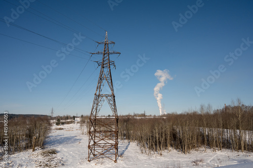Winter landscape. Sunny day. Blue sky. High voltage power line. White smoke. Naked trees. Forest.