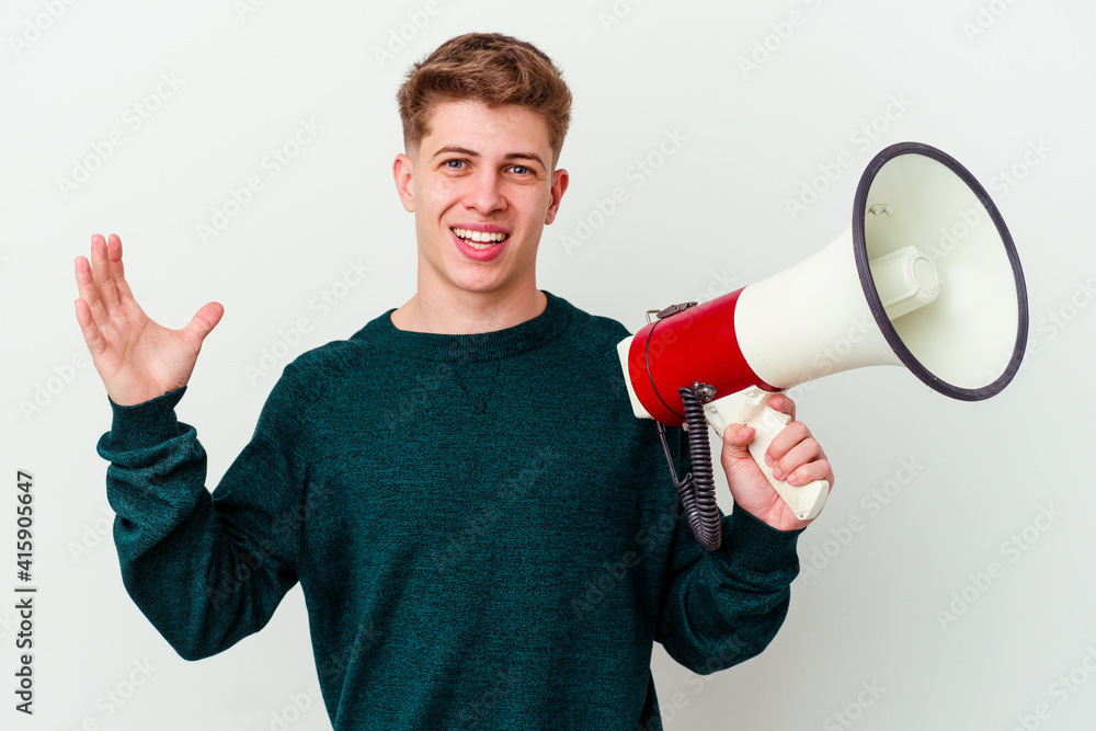 Young caucasian man holding a megaphone isolated on white background receiving a pleasant surprise, excited and raising hands. Young caucasian man holding a megaphone isolated on white background receiving a pleasant surprise, excited and raising hands.