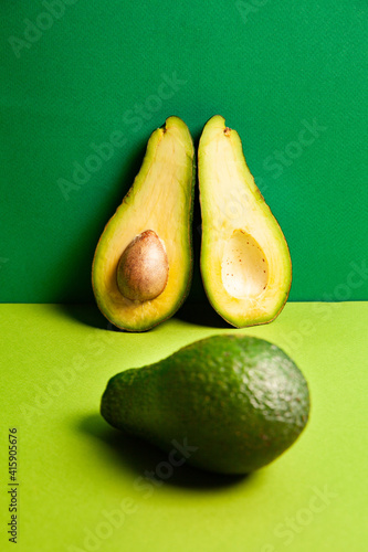 Whole ripe avocado near halved fruit against green background
