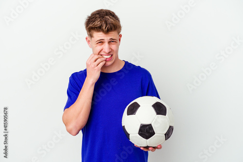 Young caucasian man playing soccer isolated on background biting fingernails, nervous and very anxious.