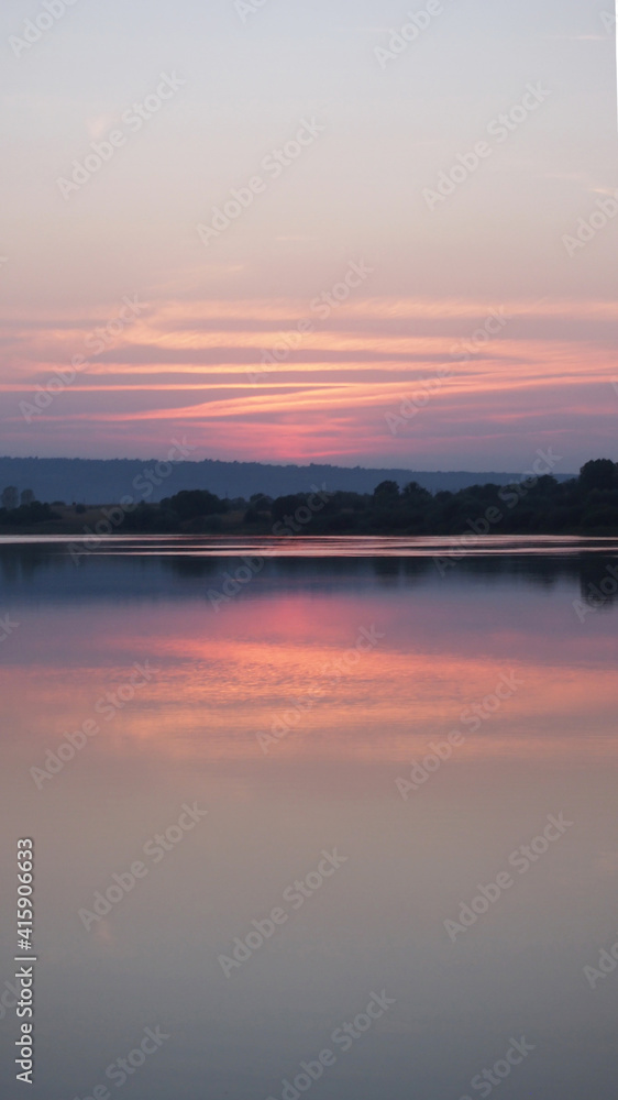 Blurry hazy image of a calm lake at sunset on a summer evening. Reflection in the water of delicate pastel colors of the sky. Artificial noise and graininess. Beauty of nature. Soft focus. Copy space