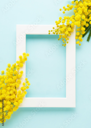 White frame with mimosa flowers on a blue background. Spring concept. Top view, copy space