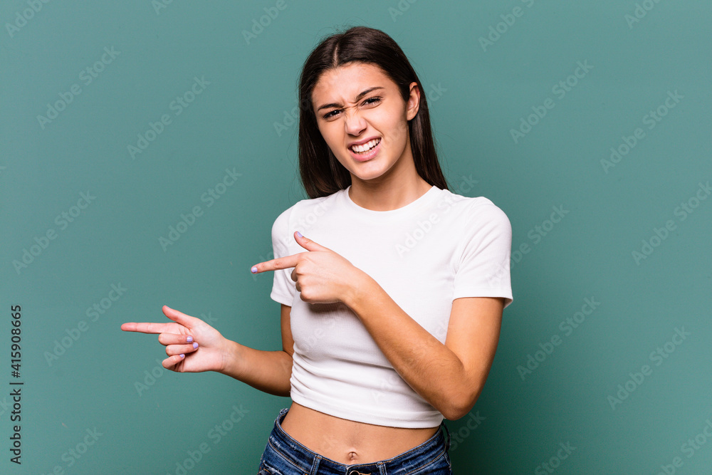 Young Indian woman isolated on blue background pointing with forefingers to a copy space, expressing excitement and desire. Young Indian woman isolated on blue background pointing with forefingers to a copy space, expressing excitement and desire.