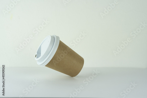 a takeaway paper cup is falling on a white table.