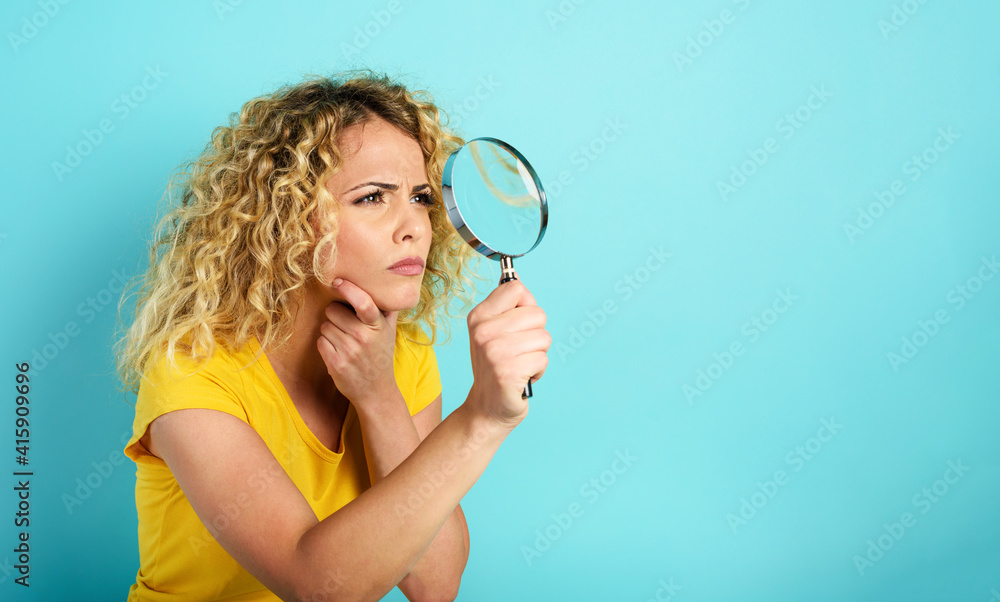 Girl with magnifier lens is distrustful about something. Cyan background Girl with magnifier lens is distrustful about something. Cyan background