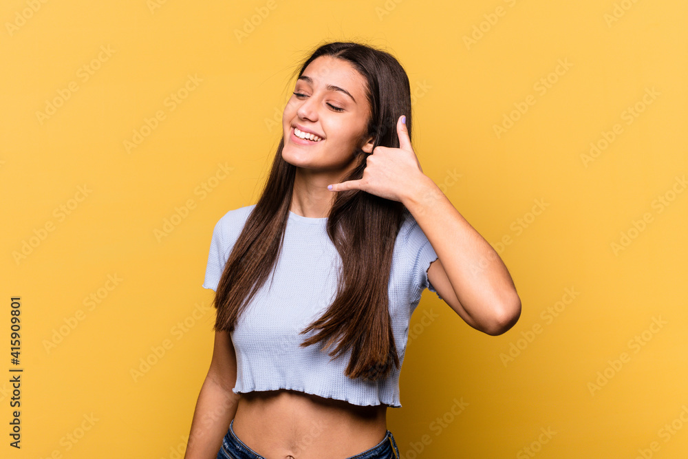 Young Indian woman isolated on yellow background showing a mobile phone call gesture with fingers. Young Indian woman isolated on yellow background showing a mobile phone call gesture with fingers.