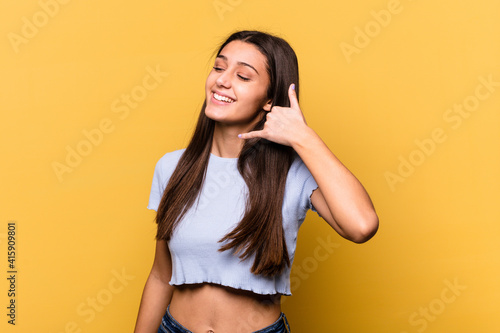 Young Indian woman isolated on yellow background showing a mobile phone call gesture with fingers.