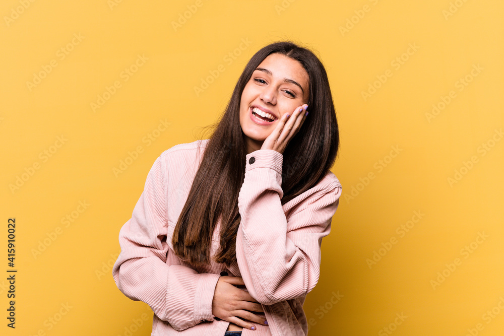 Young Indian woman isolated on yellow background laughs happily and has fun keeping hands on stomach. Young Indian woman isolated on yellow background laughs happily and has fun keeping hands on stomach.