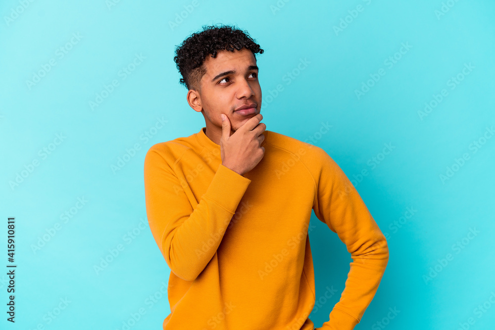 Young african american curly man isolated on blue looking sideways with doubtful and skeptical expression. Young african american curly man isolated on blue looking sideways with doubtful and skeptical expression.