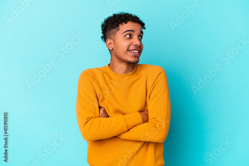 Young african american curly man isolated on blue smiling confident with crossed arms. © Asier