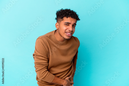 Young african american curly man isolated on blue having a liver pain, stomach ache.