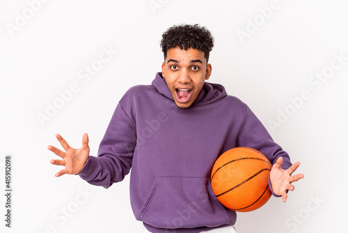 Young african american curly man isolated playing basketball receiving a pleasant surprise, excited and raising hands. © Asier