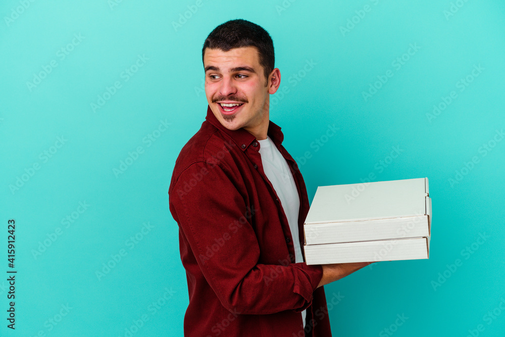 Young caucasian man holding pizzas isolated on blue background looks aside smiling, cheerful and pleasant. Young caucasian man holding pizzas isolated on blue background looks aside smiling, cheerful and pleasant.