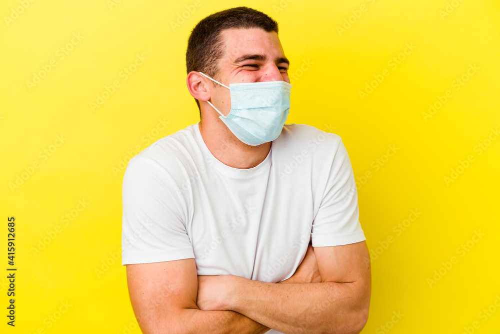 Young caucasian man wearing a protection for coronavirus isolated on yellow background laughing and having fun.