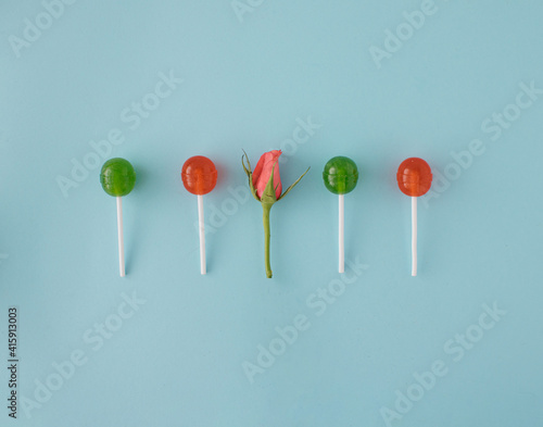 Lollipops, various colors, red and green in line with pink rose on pastel blue background. Be different. Be romantic. Minimal creative concept © DV Imaginarium