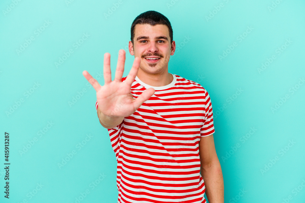 Young caucasian man isolated on blue background smiling cheerful showing number five with fingers. Young caucasian man isolated on blue background smiling cheerful showing number five with fingers.