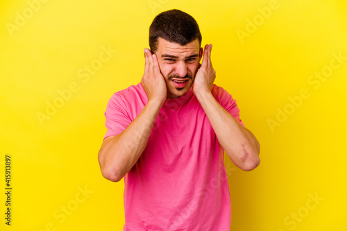 Young caucasian cool man isolated on yellow background covering ears with fingers, stressed and desperate by a loudly ambient. © Asier